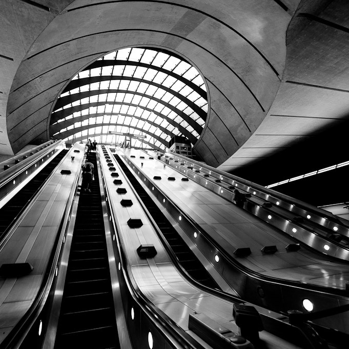 Escalators rising through a curved concrete tunnel at Canary Wharf Jubilee line station